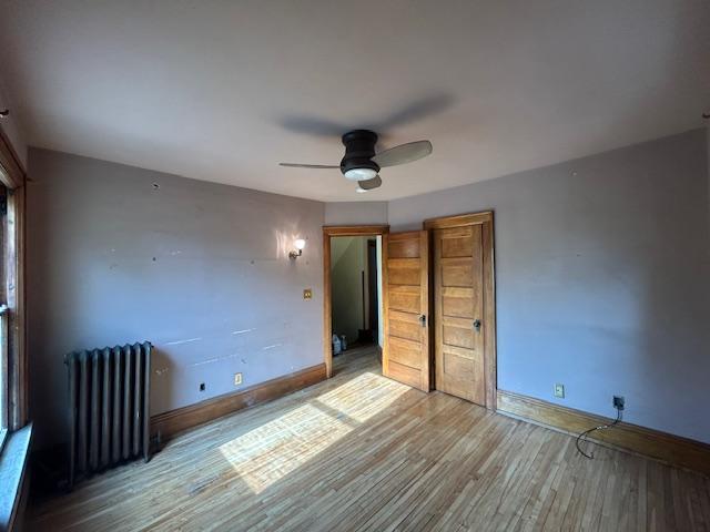 unfurnished bedroom with radiator heating unit, wood finished floors, baseboards, and a ceiling fan