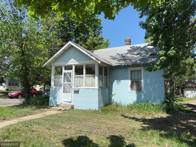 2224 42nd St, Minneapolis, MN 55407 - bungalow-style home featuring a sunroom, a chimney, stucco siding, roof with shingles, and a front lawn