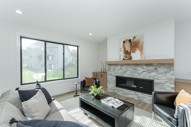 living area featuring light wood-style flooring, a stone fireplace, recessed lighting, and baseboards