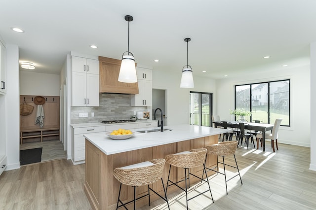 kitchen featuring a sink, gas stovetop, tasteful backsplash, white cabinetry, and a breakfast bar area