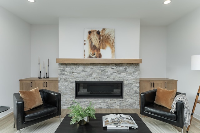 living area with wood finished floors, recessed lighting, a stone fireplace, and baseboards