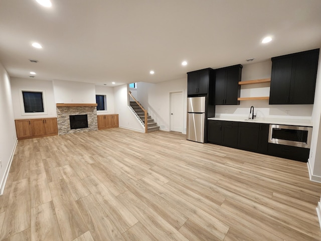 unfurnished living room featuring a stone fireplace, baseboards, stairs, light wood-style floors, and recessed lighting