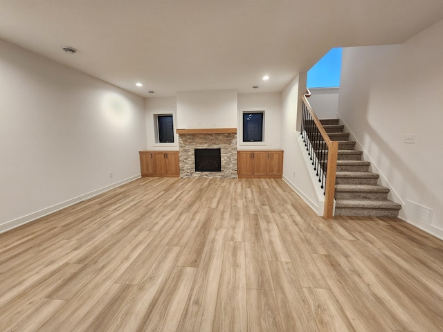 unfurnished living room featuring stairway, light wood-style flooring, a stone fireplace, recessed lighting, and baseboards