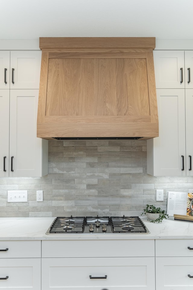 kitchen with stainless steel gas cooktop, custom range hood, tasteful backsplash, and white cabinets
