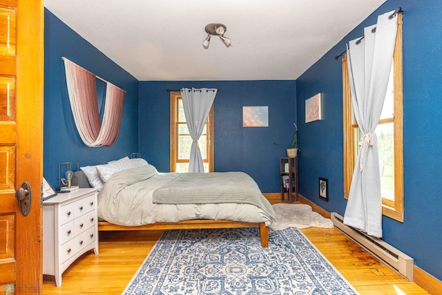 bedroom featuring baseboard heating, light wood-style flooring, and baseboards