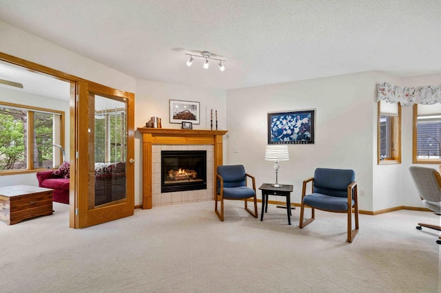 carpeted living area featuring a tiled fireplace, baseboards, and a textured ceiling