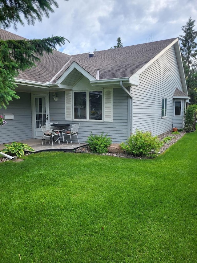 rear view of house with roof with shingles, a lawn, and a patio