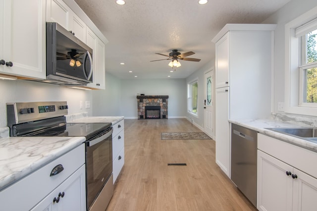 504 Wisconsin Ave N, Frederic, WI 54837 - kitchen featuring stainless steel appliances, a fireplace, light wood finished floors, white cabinets, and a ceiling fan