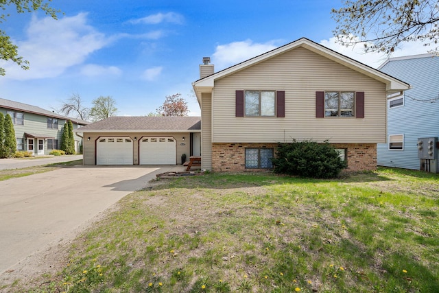 split level home featuring an attached garage, concrete driveway, a chimney, brick siding, and a front yard