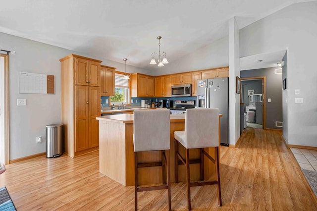 kitchen with appliances with stainless steel finishes, light wood-type flooring, light countertops, a kitchen island, and decorative light fixtures