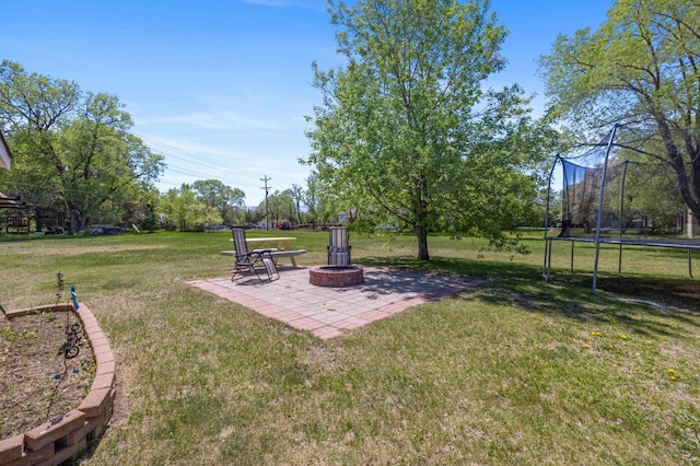 view of grassy yard featuring a trampoline, a patio, and a fire pit