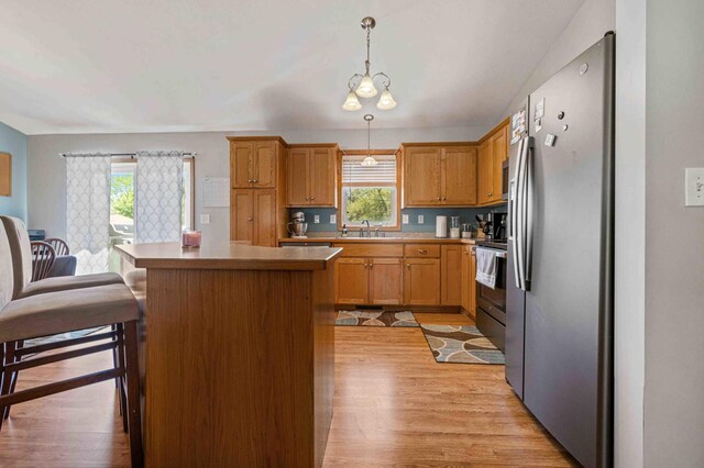 kitchen featuring appliances with stainless steel finishes, a sink, a center island, light wood-type flooring, and healthy amount of natural light