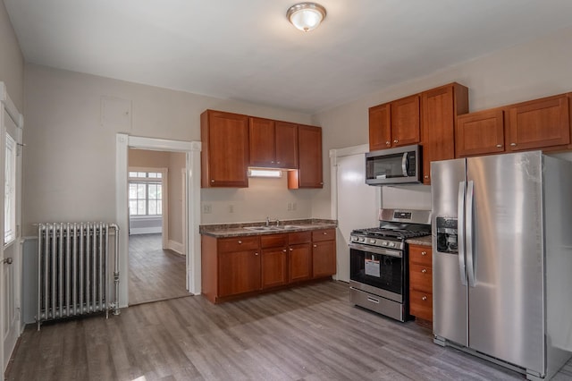 410 Baker St W, Saint Paul, MN 55107 - kitchen featuring stainless steel appliances, radiator heating unit, a sink, wood finished floors, and brown cabinetry