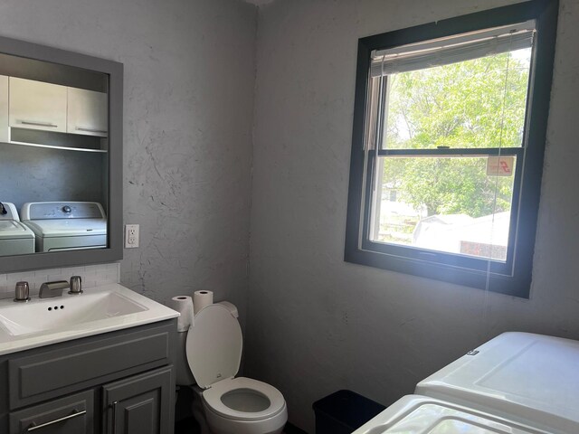 half bath featuring independent washer and dryer, toilet, healthy amount of natural light, and vanity