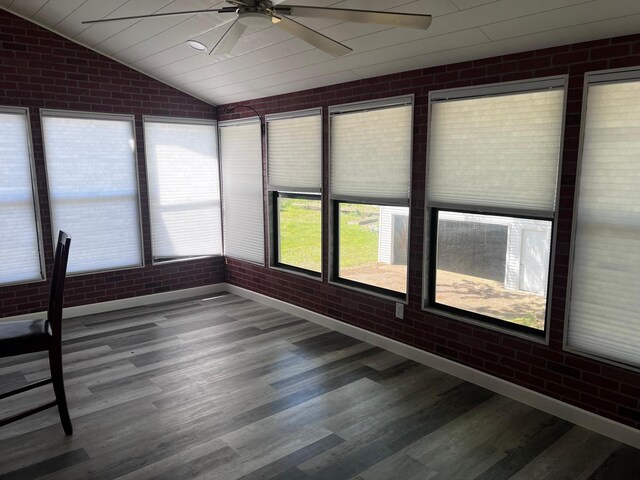 unfurnished sunroom featuring ceiling fan, brick wall, wood finished floors, and lofted ceiling