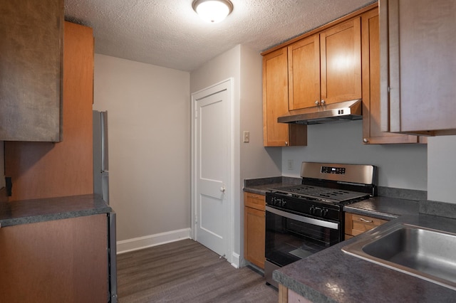 kitchen with stainless steel appliances, under cabinet range hood, dark wood-type flooring, dark countertops, and a textured ceiling