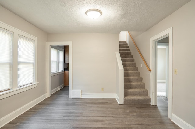 spare room featuring a textured ceiling, wood finished floors, stairway, and baseboards