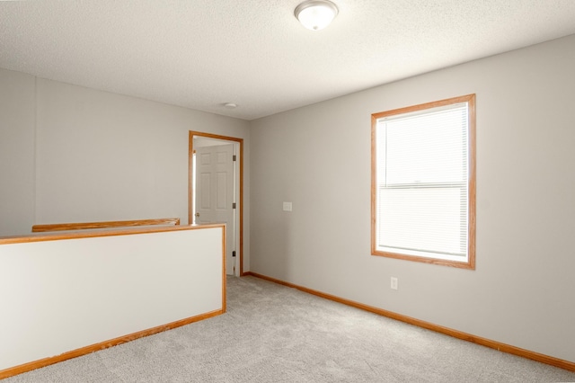 empty room featuring light colored carpet, baseboards, and a textured ceiling