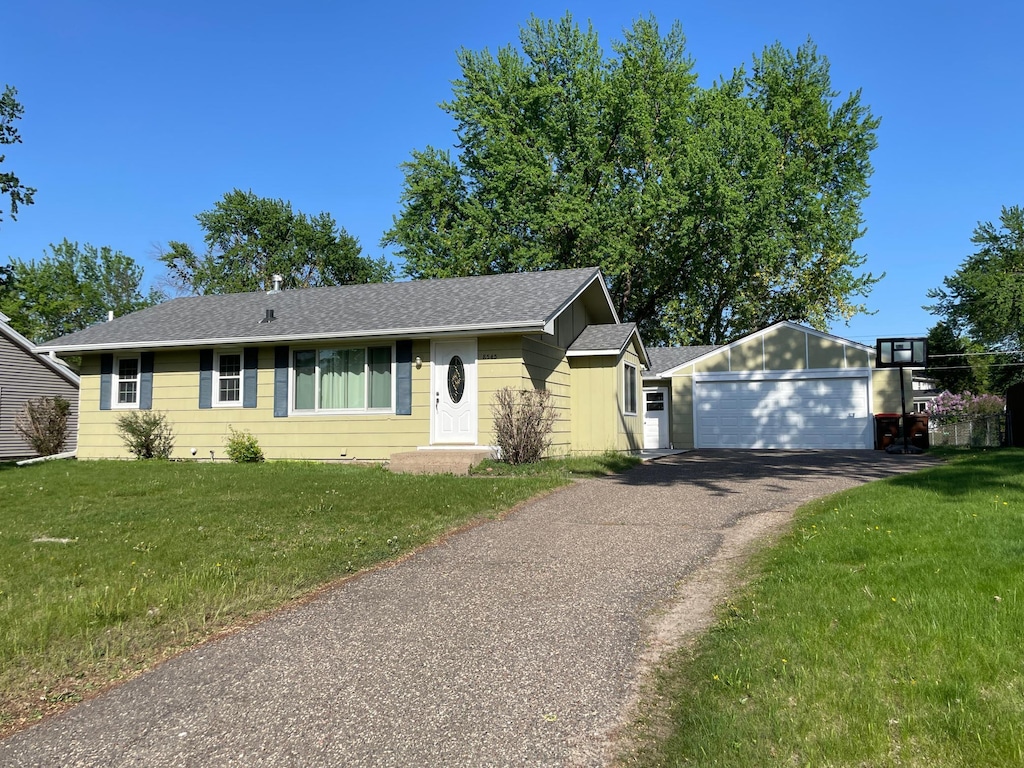 ranch-style house featuring a detached garage, a front yard, roof with shingles, and an outbuilding