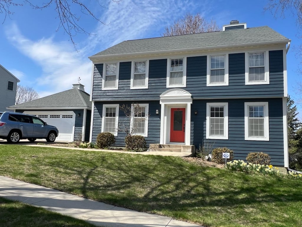 colonial inspired home featuring a chimney, an attached garage, and a front yard