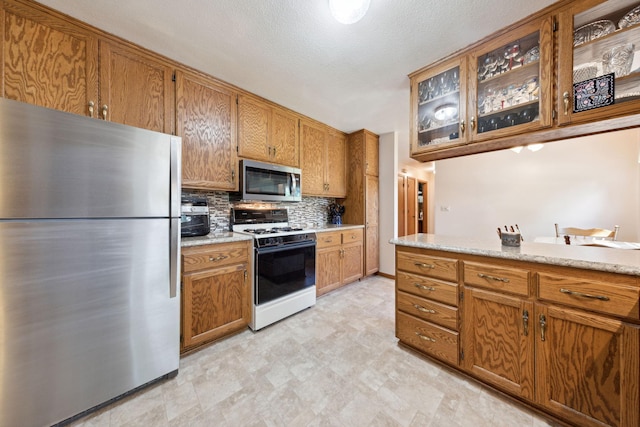 6420 Rolling Hills Rd, Corcoran, MN 55340 - kitchen with appliances with stainless steel finishes, brown cabinetry, backsplash, glass insert cabinets, and light floors