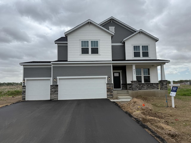 view of front of home with stone siding, driveway, a porch, and a garage