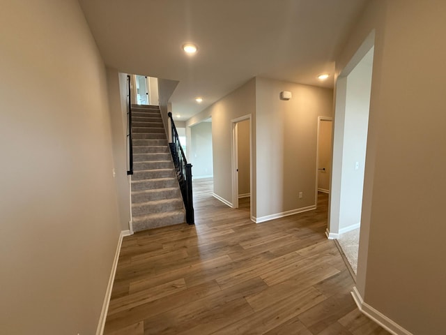 hall featuring wood finished floors, baseboards, stairs, and recessed lighting