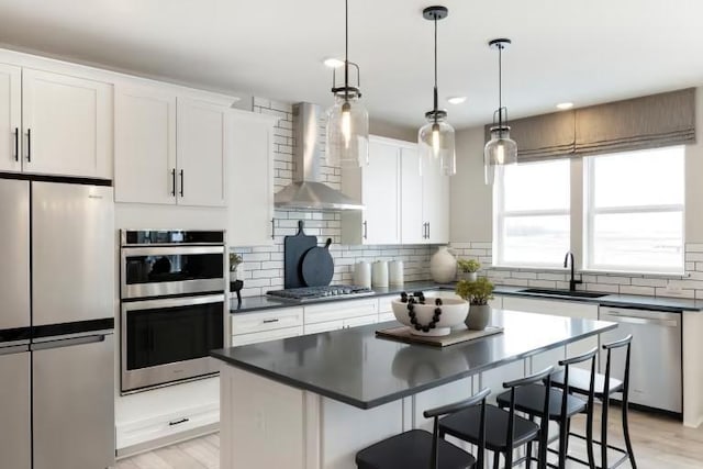 kitchen featuring stainless steel appliances, wall chimney exhaust hood, a sink, dark countertops, and recessed lighting