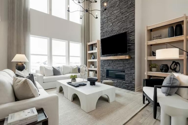 living room with a high ceiling, a stone fireplace, a chandelier, and light wood-style floors