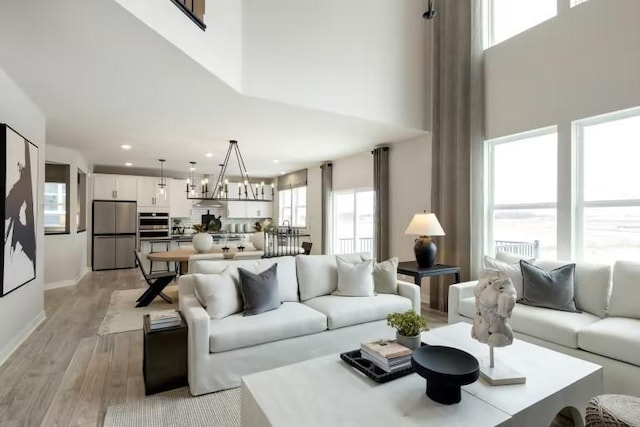 living room featuring a towering ceiling, healthy amount of natural light, light wood finished floors, recessed lighting, and baseboards