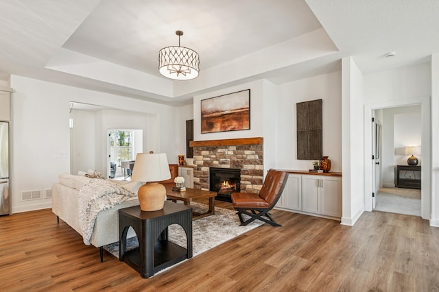 14633 Packard St NE, Ham Lake, MN 55304 - living area featuring a raised ceiling, light wood-style floors, a stone fireplace, and a chandelier