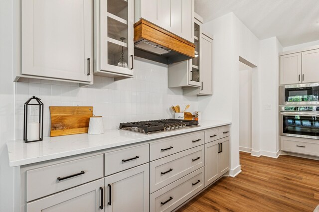14633 Packard St NE, Ham Lake, MN 55304 - kitchen featuring stainless steel appliances, decorative backsplash, wood finished floors, glass insert cabinets, and light stone countertops