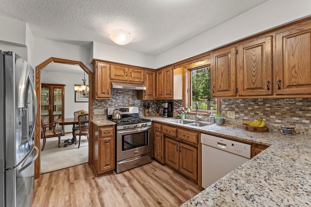9755 Egret Blvd NW, Coon Rapids, MN 55433 - kitchen featuring appliances with stainless steel finishes, under cabinet range hood, brown cabinetry, light wood finished floors, and tasteful backsplash