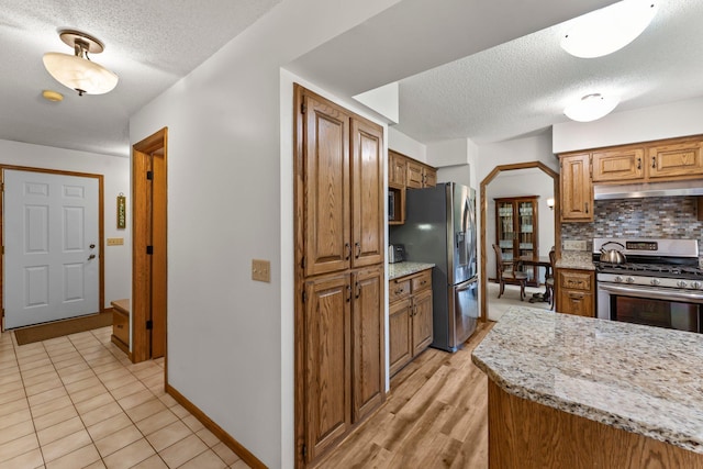 9755 Egret Blvd NW, Coon Rapids, MN 55433 - kitchen featuring stainless steel appliances, a textured ceiling, under cabinet range hood, decorative backsplash, and arched walkways