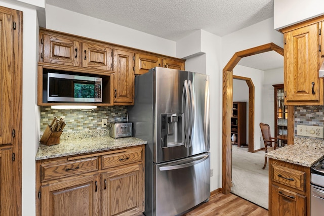 9755 Egret Blvd NW, Coon Rapids, MN 55433 - kitchen with appliances with stainless steel finishes, light wood-type flooring, arched walkways, tasteful backsplash, and a textured ceiling