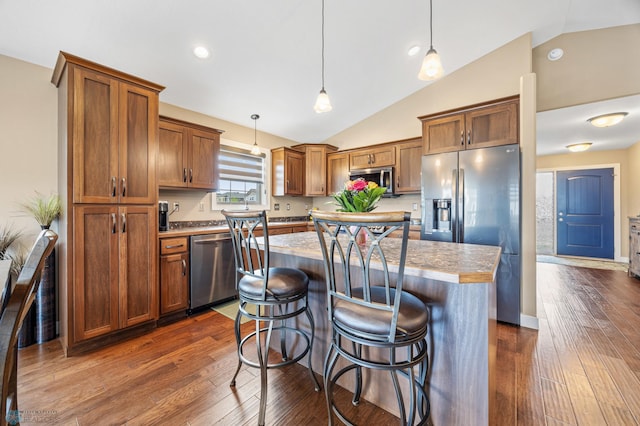 5409 47th Ave S, Fargo, ND 58104 - kitchen featuring stainless steel appliances, vaulted ceiling, brown cabinets, dark wood finished floors, and a kitchen island