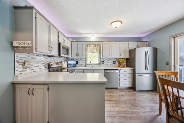 1435 104th Ln NW, Coon Rapids, MN 55433 - kitchen featuring stainless steel appliances, a sink, a peninsula, light wood-style floors, and a textured ceiling