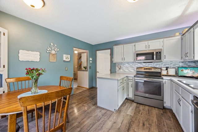 1435 104th Ln NW, Coon Rapids, MN 55433 - kitchen featuring stainless steel appliances, light countertops, backsplash, a peninsula, and dark wood-style floors