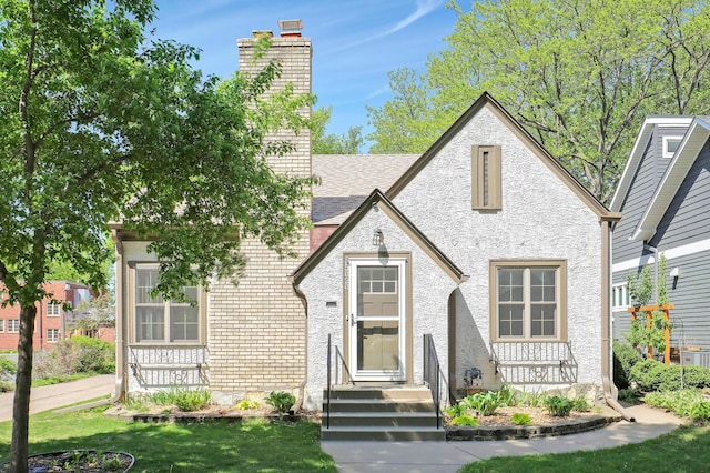 view of front of house featuring a chimney, roof with shingles, a front lawn, and stucco siding