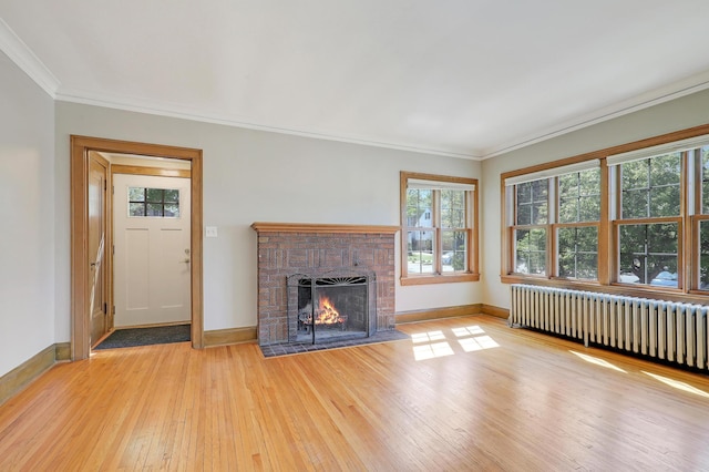 unfurnished living room featuring radiator, light wood-type flooring, a brick fireplace, baseboards, and crown molding