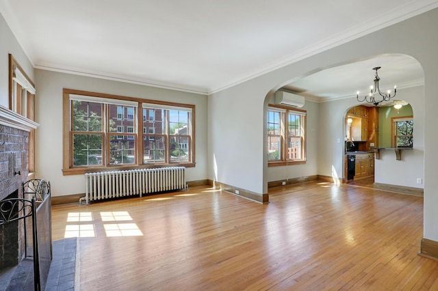 unfurnished living room with radiator, arched walkways, an AC wall unit, light wood-style floors, and crown molding