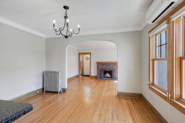 unfurnished living room with radiator heating unit, an AC wall unit, arched walkways, a chandelier, and baseboards