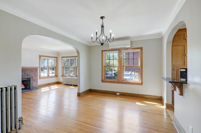 unfurnished living room featuring radiator heating unit, a wall mounted AC, light wood finished floors, a chandelier, and crown molding