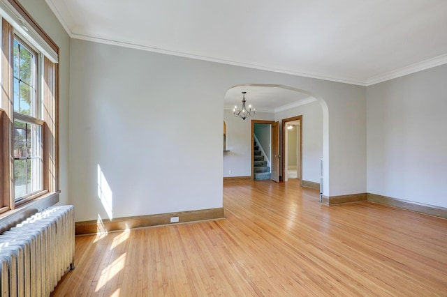 empty room featuring radiator heating unit, arched walkways, light wood-type flooring, stairway, and plenty of natural light