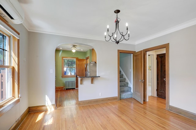 spare room with radiator, arched walkways, a wall unit AC, stairs, and light wood-style flooring