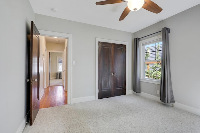 unfurnished bedroom with carpet floors, baseboards, a closet, ceiling fan, and radiator heating unit