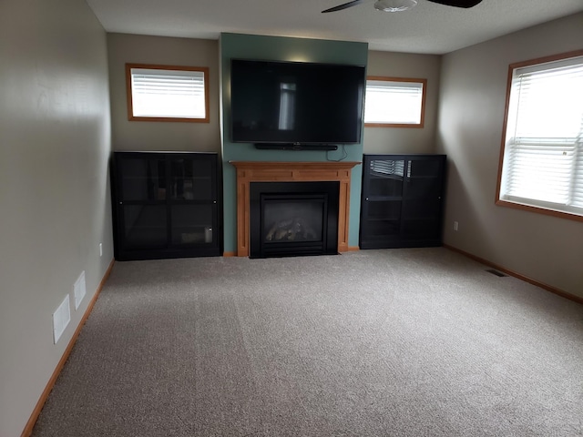 unfurnished living room featuring a glass covered fireplace, a ceiling fan, carpet flooring, and baseboards