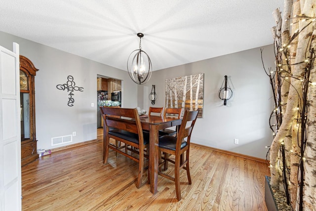 dining room featuring light wood finished floors, a chandelier, baseboards, and a textured ceiling