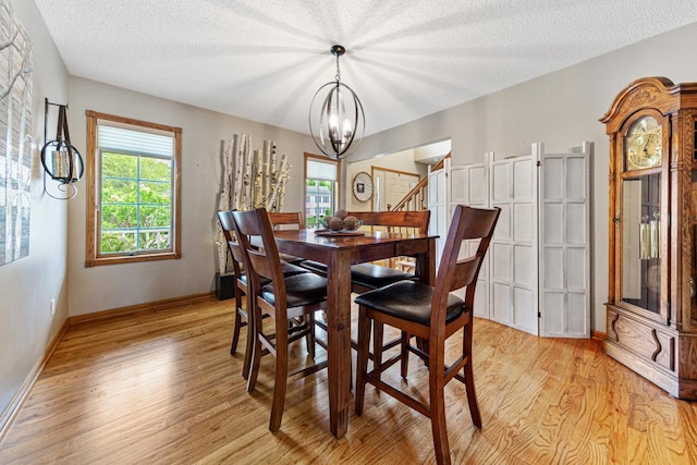 dining space featuring a chandelier, light wood-style floors, a textured ceiling, and baseboards