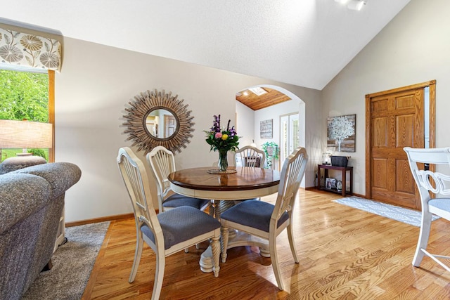dining space with arched walkways, healthy amount of natural light, light wood-style flooring, high vaulted ceiling, and baseboards